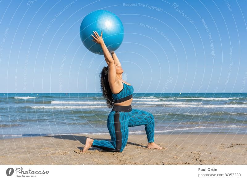 Frau spielt mit einem Fitnessball und macht Sportübungen am Strand Ball jung Erwachsener lateinamerikanisch Afro-Look Amerikaner Yoga Plus Konfektionsgröße