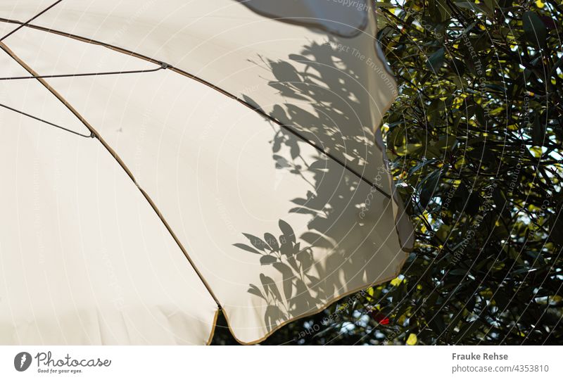 Teil eines weißen Sonnenschirms mit Schatten von Blättern eines Baumes hinter ihm sonnig Sommerstimmung Garten im Schatten Licht Schattenspiel Kontrast