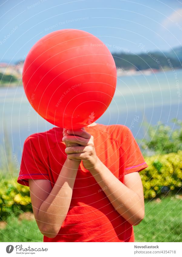 Junge versteckt sein Gesicht hinter einem roten Luftballon allein Hintergrund Geburtstag lässig Freizeitbekleidung Kaukasier feiern Feier Kind Kindheit