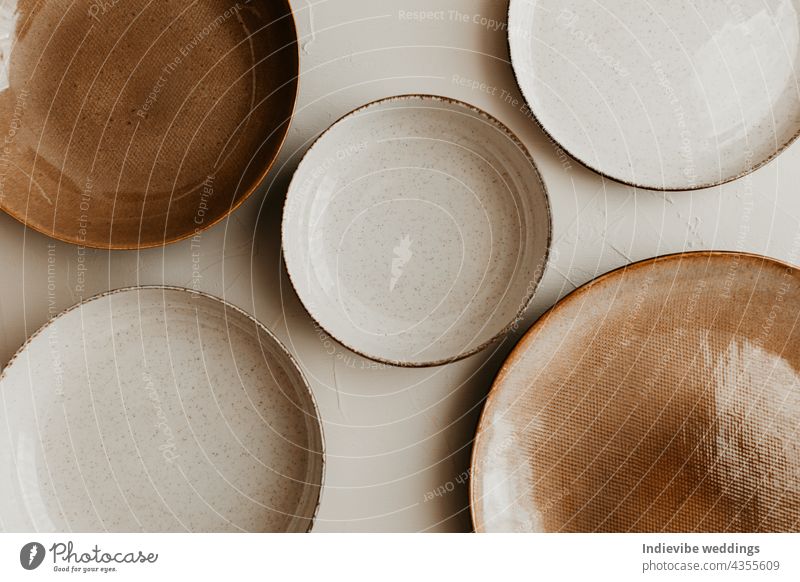 Fünf unterschiedlich große Teller auf beigem Hintergrund. Texturiertes, körniges Muster auf den Tellern. Flachlage, Ansicht von oben. Braune und naturfarbene Teller.