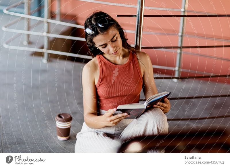 Eine Studentin sitzt auf einer Treppe auf dem Campus und liest ein Buch, neben ihr steht ein Glas Kaffee Schüler Mädchen Sitzen lesen Lernen Hochschule Schule