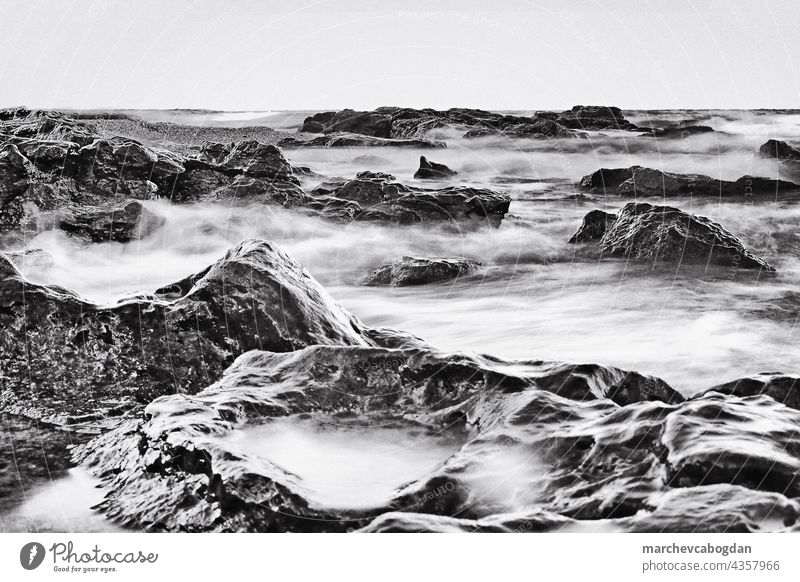 Langzeitbelichtung des über große Kieselsteine fließenden Meeres. Monochromes Bild. Felsen Natur Wasser Küste Landschaft winken Detailaufnahme Strand Stein
