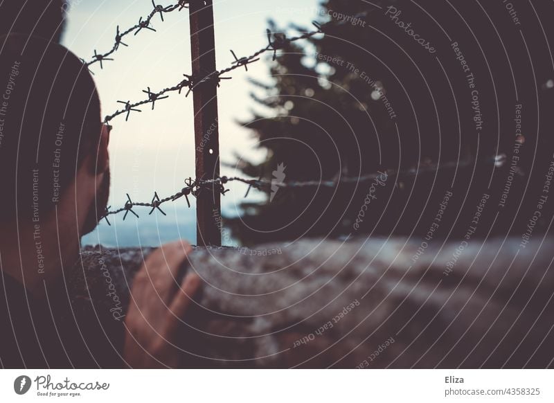 Mann Blick über einen Zaun mit Stacheldraht. Konzept Gefangen sein und Fernweh. gefangen Gefängnis Stacheldrahtzaun Grenze Barriere Sicherheit Freiheit Verbote