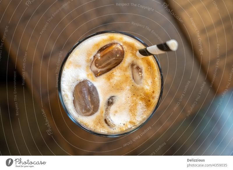 Blick von oben auf einen Eiskaffee mit Strohhalm auf einem Holztisch Kaffee Latte Kaffee-Latte melken kalt trinken Eiswürfel Café Kantine Koffein Nahaufnahme