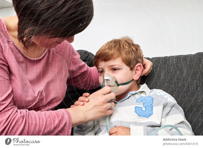 Mutter, die ihrem Kind eine Sauerstoffmaske zum Einatmen aufs Gesicht setzt Mundschutz angezogen inhalieren Verfahren krank Zusammensein heimwärts Sohn Eltern
