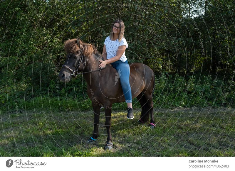 Junge Frau sitzt zufrieden auf einem Islandpferd Mensch Erwachsene Außenaufnahme Pferd Isländer Pony brünett 18-30 Jahre Farbfoto Blick in die Kamera langhaarig