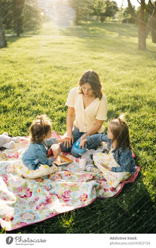 Fröhliche Mutter und Kinder beim Picknick im Park Zusammensein Sommer Glück Liebe Tochter Geschwisterkind trinken Tasse Mama Partnerschaft wenig Schwester