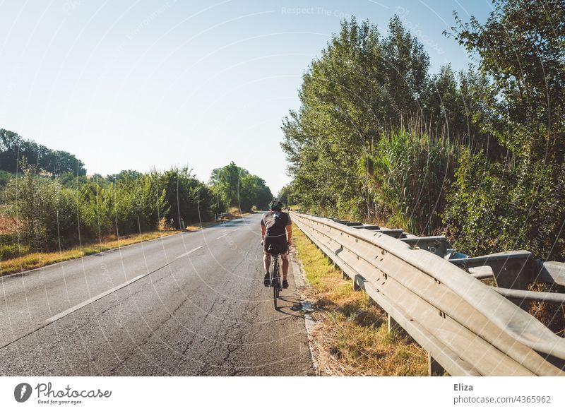 Rennradfahrer in Sportbekleidung fährt mit seinem Fahrrad auf einer italienischen Landstraße Fahrradfahrer Italien mediterran Sommer Urlaub Fahrradfahren