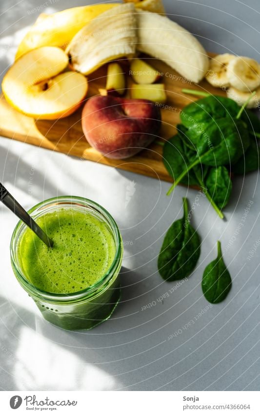 Grüner Smoothie in einem Trinkglas und Zutaten auf einem Holz Schneidebrett smoothie grün Obst Gemüse Vegetarische Ernährung Gesunde Ernährung selbstgemacht