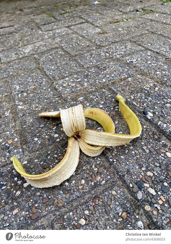 Achtung Rutschgefahr... Achtlos weggeworfene Bananenschale liegt auf einem Gehweg... ausrutschen gefährlich Unfall Pflastersteine liegen Biomüll Bürgersteig