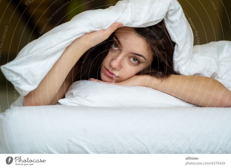 Porträt einer attraktiven, jungen, sexy braunhaarigen Frau im Bett, Hand und Kopf auf dem Kopfkissen unter der Decke, Raum kopieren. Lifestyle aussruhen hübsch