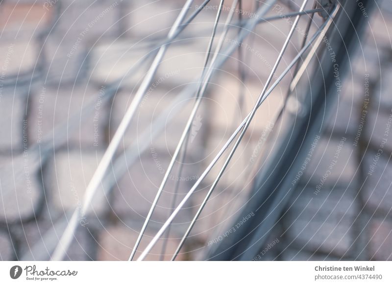 Blick durch die Speichen eines Fahrrades auf schönes Kopfsteinpflaster. Nahaufnahme mit viel Unschärfe Fahrradspeichen Vorderrad von oben Pflastersteine
