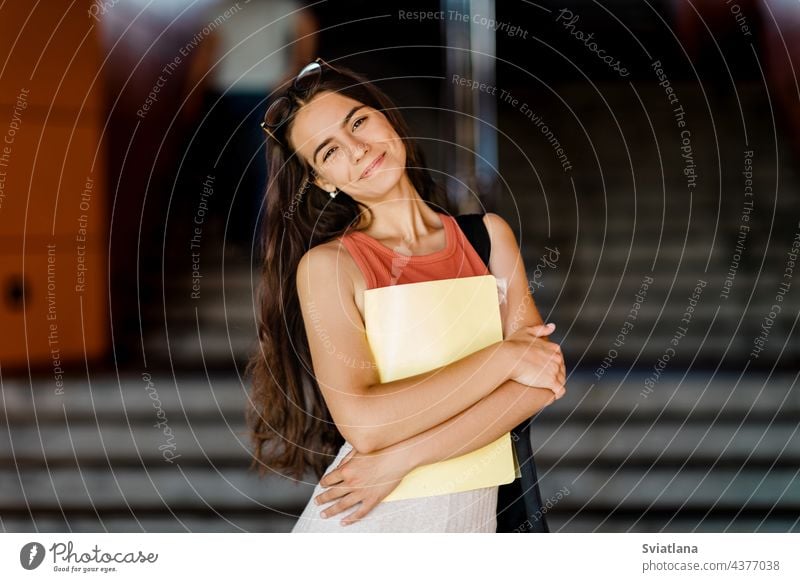 Porträt eines lächelnden Mädchens mit einer Mappe in den Händen Schüler Freitreppe Lächeln Beteiligung Tasche jung Universität Treppe Brille im Freien