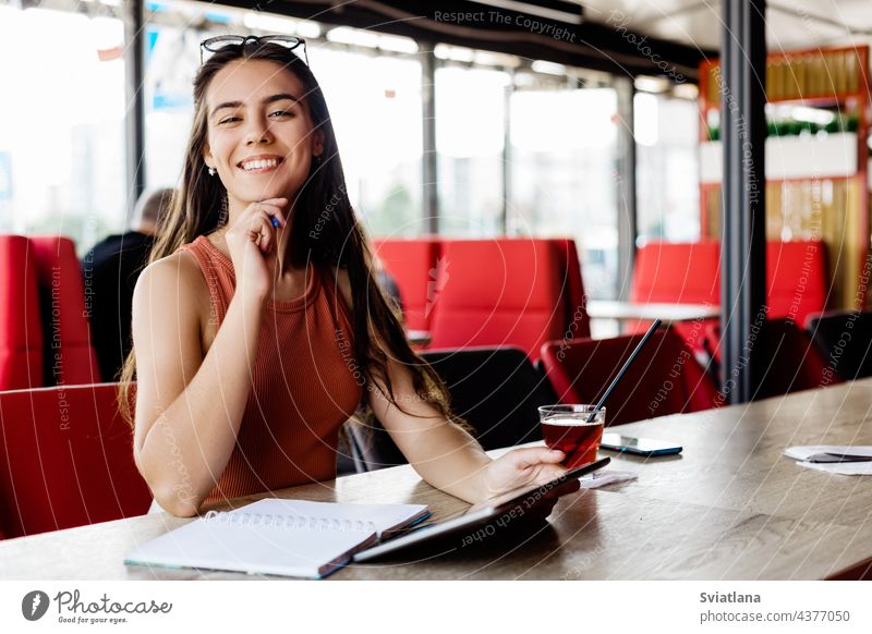 Ein schönes Mädchen mit einem Notebook und einem Tablet sitzt in einem Café und studiert oder arbeitet Notizblock Tablette Schüler Freiberufler Pause Bildung