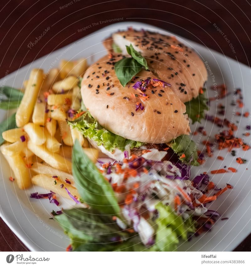 Hähnchen-Burger mit Pommes frites und Mayo-Sauce und Gemüse-Dressing auf einem Tisch Cheeseburger Beteiligung Salat ungesund schnell Fotografie Frau horizontal