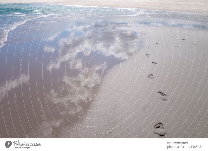 Strand nassen Sand mit frischen menschlichen nackten Fußspuren und blaue Wolke Himmel Reflexion und Wasser Wellen