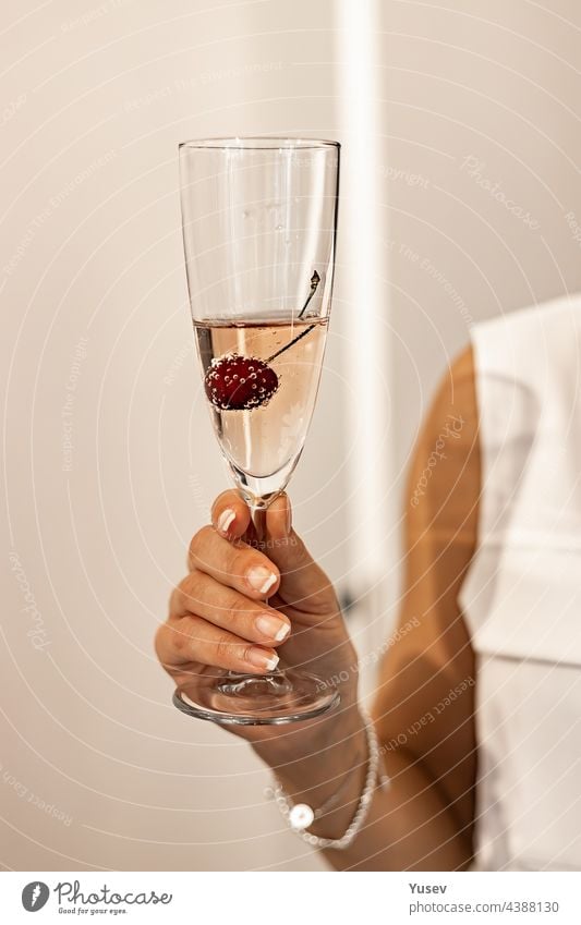 Elegante Frauenhand mit französischer Maniküre hält ein Glas Champagner oder Rosensekt. Menschliche Hände. Urlaubs- oder Veranstaltungskonzept. Vertikale Aufnahme