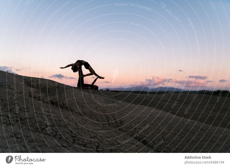 Flexibles Paar übt Acro-Yoga bei Sonnenuntergang Akro-Yoga akrobatisch Gleichgewicht abstützen Partner Zusammensein Berge u. Gebirge Himmel Partnerschaft Abend