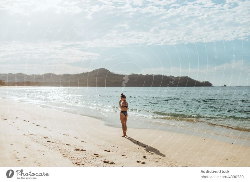 Junge Frau steht am Sandstrand Strand Meer allein Sommer Sonnenlicht Natur reisen MEER Urlaub Küste jung Meeresufer Feiertag Ufer winken Bikini Seeküste
