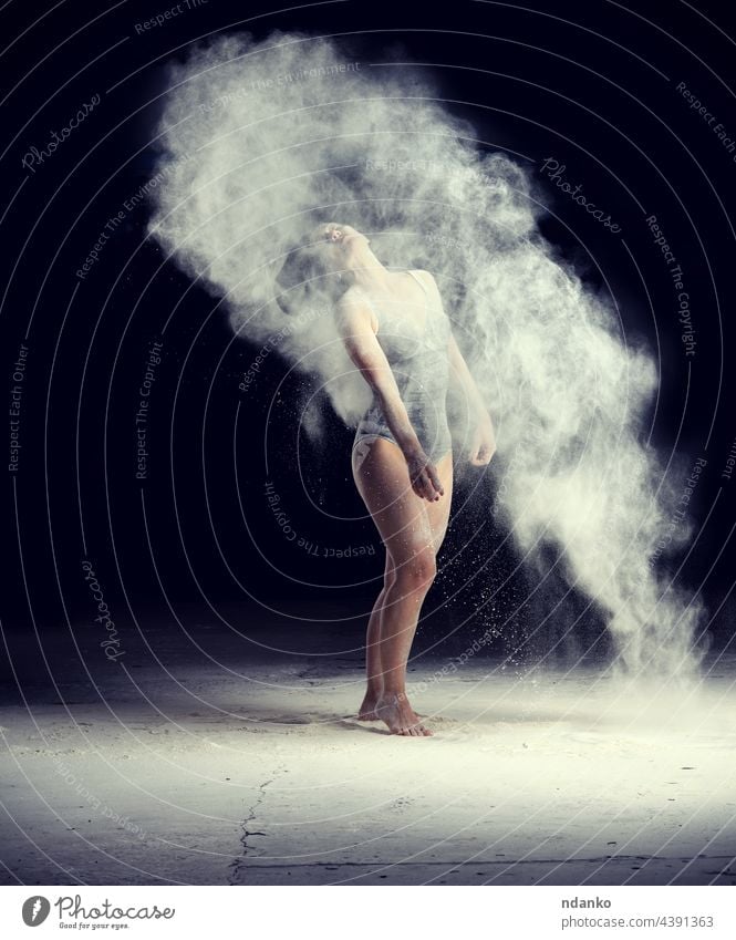 schöne kaukasische Frau im schwarzen Bodysuit mit sportlicher Figur tanzt in einer weißen Mehlwolke auf schwarzem Hintergrund Aktion aktiv Erwachsener Kunst