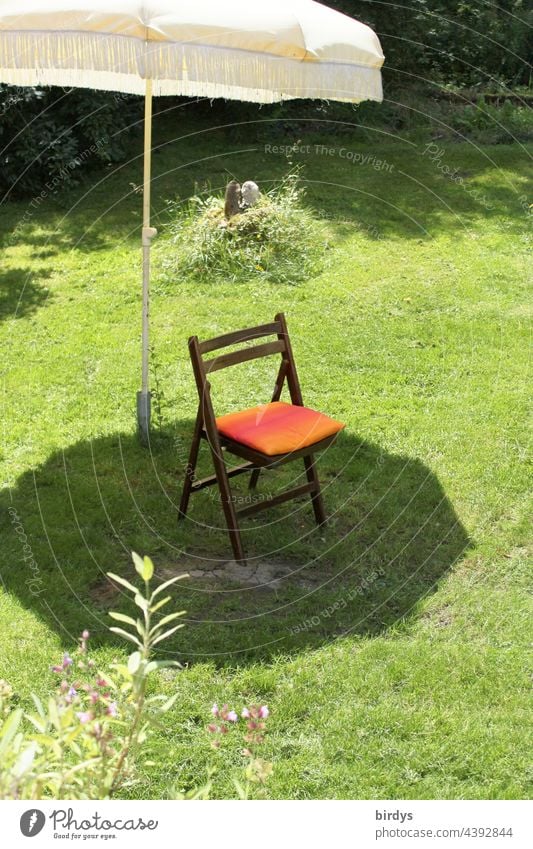 Einzelner Stuhl im Schatten eines Sonnenschirms auf einem Rasen. Schattenplatz Sonnenlicht Garten Hitze Schönes Wetter Gras Klappstuhl Sitzplatz Sommer