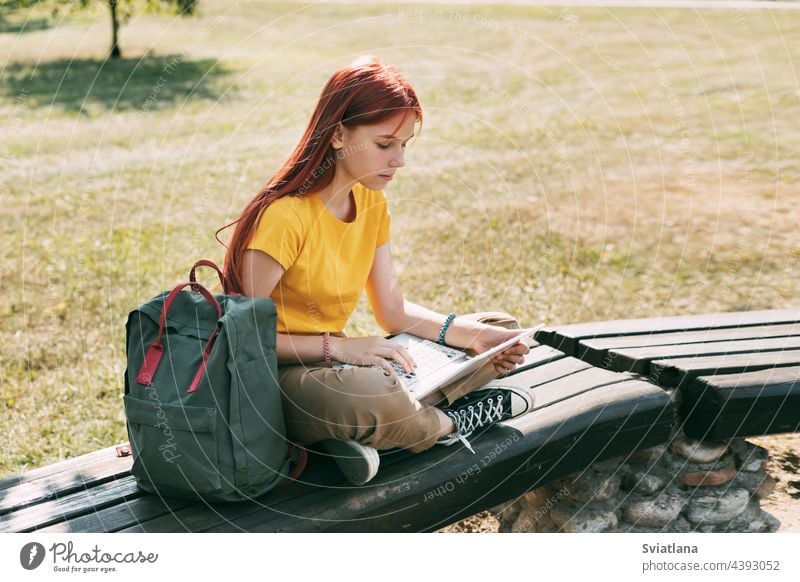 Ein junges Mädchen sitzt mit einem Laptop auf einer Parkbank und bereitet sich auf den Unterricht oder Prüfungen vor. Das Konzept der Ausbildung und Bildung
