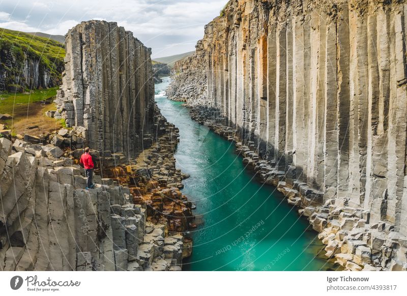 Wanderer in roter Jacke beim Besuch der Studlagil-Basaltschlucht mit seltenen vulkanischen Basaltsäulenformationen, Island Schlucht Mann studlagil Spalte