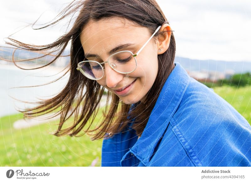 Zufriedene Frau auf einem Hügel am Meer sitzend MEER genießen Seeküste wolkig bewundern Lächeln Strandpromenade Harmonie Natur Himmel grün heiter Glück Küste