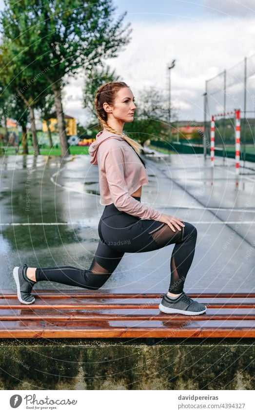 Junge Sportlerin streckt die Beine im Freien strecken auf einer Bank Boxerflechten Frau Athlet Körper Aufwärmen Training geduckt trainiert. sportlich Sweatshirt