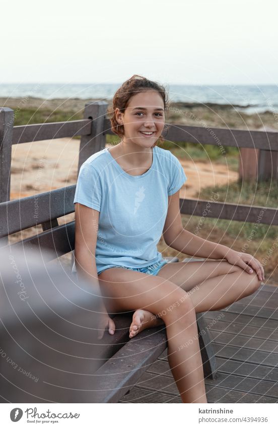 Lächelndes Teenager-Mädchen sitzt auf einer Holzbank in der Nähe der Küste im Freien MEER Bank Sonnenuntergang Attrappe blau hölzern Kaukasier Jugendlicher