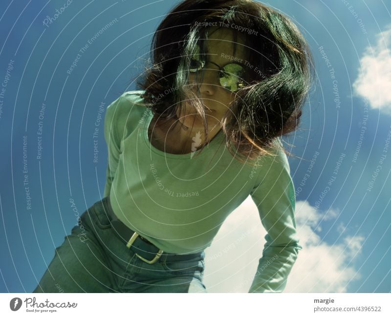 Eine Frau mit Sonnenbrille schaut nach unten in die Kamera. Über ihr ein blauer Himmel mit Wolken Junge Frau Haare & Frisuren Gesicht Porträt feminin Mensch