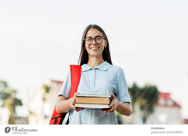Eine fröhliche Studentin mit Rucksack und Büchern, die auf der Straße steht und lächelt Schüler Lächeln Buch Universität Mädchen heiter Park Stehen attraktiv