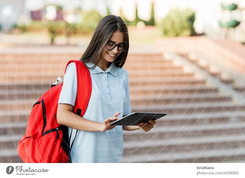 Eine Studentin schreibt eine Nachricht auf ihrem Tablet, während sie durch die Stadt läuft Mädchen Schüler Tablette lernen Rucksack Treppe Brille Lächeln