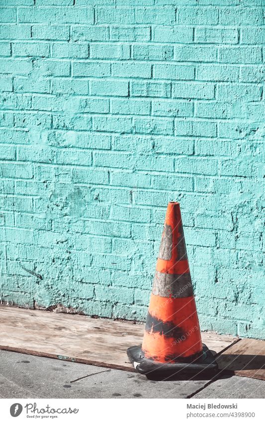 Alter schmutziger Verkehrsleitkegel an einer Backsteinmauer, selektiver Fokus, angewandte Farbtonung. Straße alt Zapfen Großstadt Sicherheit Gefahr Ermahnung