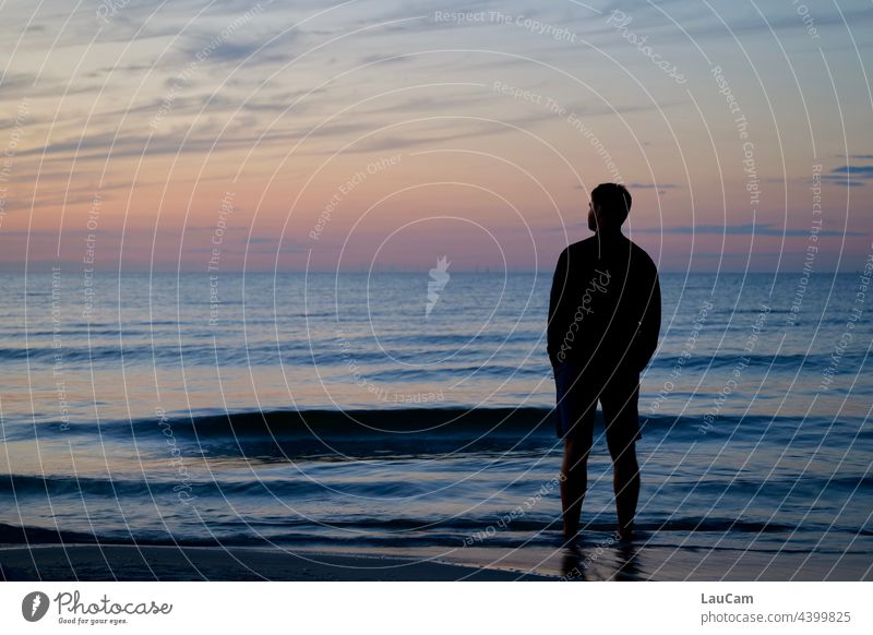 Die Sonne ist gerade untergegangen. In der Abendstimmung steht ein Mann am Strand im Wasser und blickt in die Ferne... Sonnenuntergang Dämmerung
