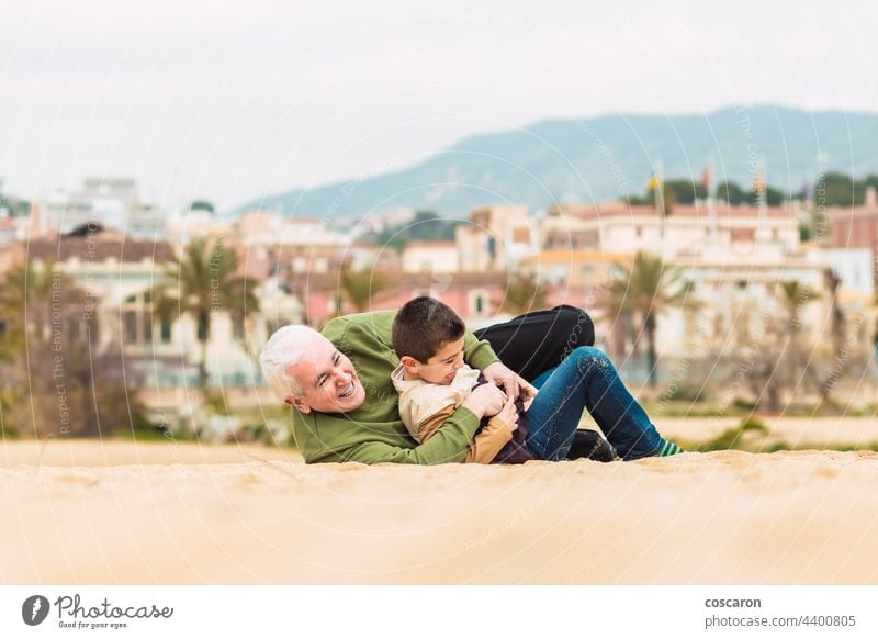 Lustiger Junge und sein Großvater spielen ausgestreckt im Sand am Strand aktiv Kaukasier Kind Kindheit niedlich el masnou Familie Spaß Generation Generationen