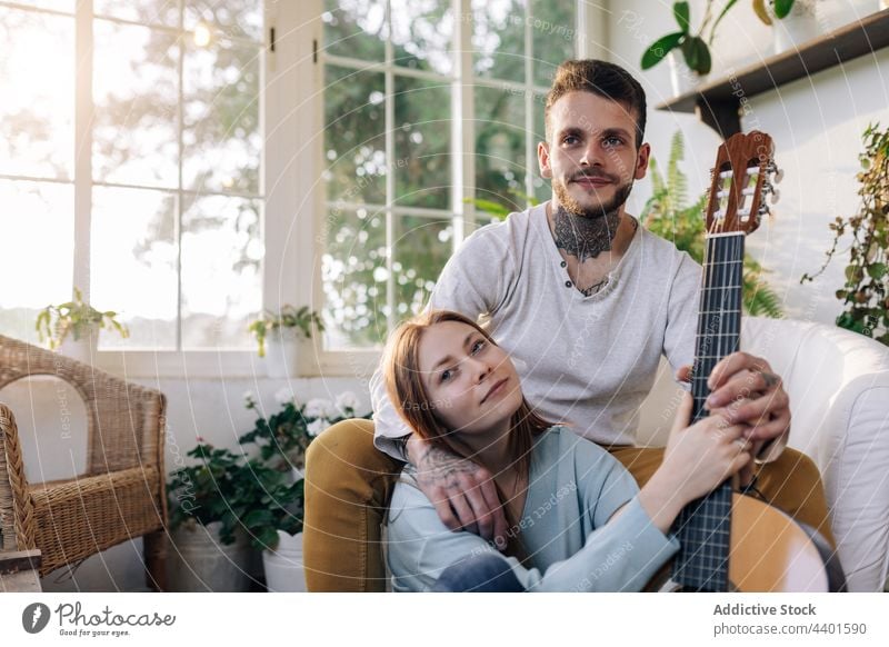 Lächelnder Gitarrist spielt Gitarre, während er mit seinem Freund zu Hause interagiert Gitarrenspieler Freundin spielen interagieren Partnerschaft Liebe Musik