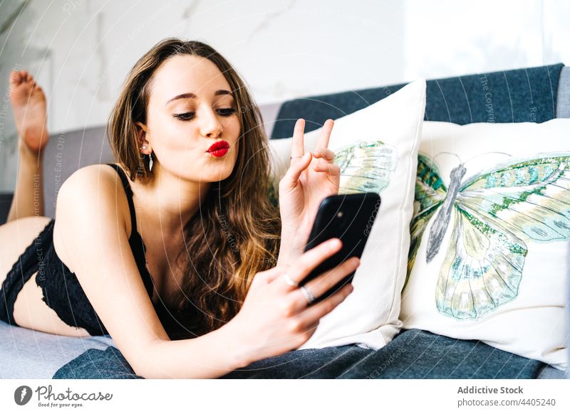 Fröhliche Frau in Unterwäsche, die im Wohnzimmer auf ihrem Smartphone surft Browsen Dessous benutzend Nachricht heiter Sofa heimwärts Mobile soziale Netzwerke