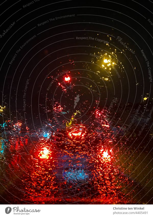 Blick durch die regennasse Windschutzscheibe auf beleuchtete Autos, die in der Dunkelheit an einer Ampel warten Regen Lichter im Regen Autolichter verregnet