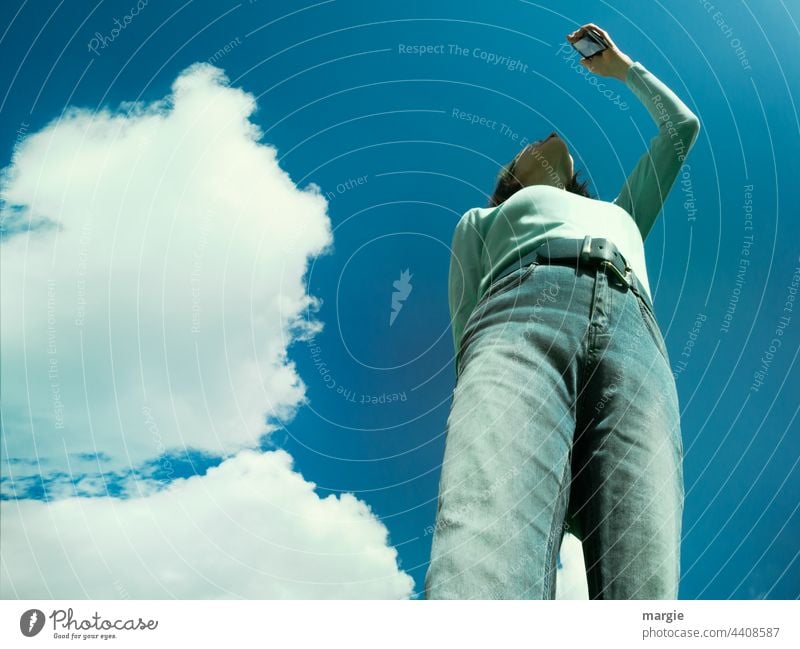 Himmel, Wolken, eine Frau sucht die Verbindung in ihrem Smartphone, Handy Blauer Himmel Sonne Schönes Wetter handyfoto Sonnenlicht Jeanshose jeans Gürtel