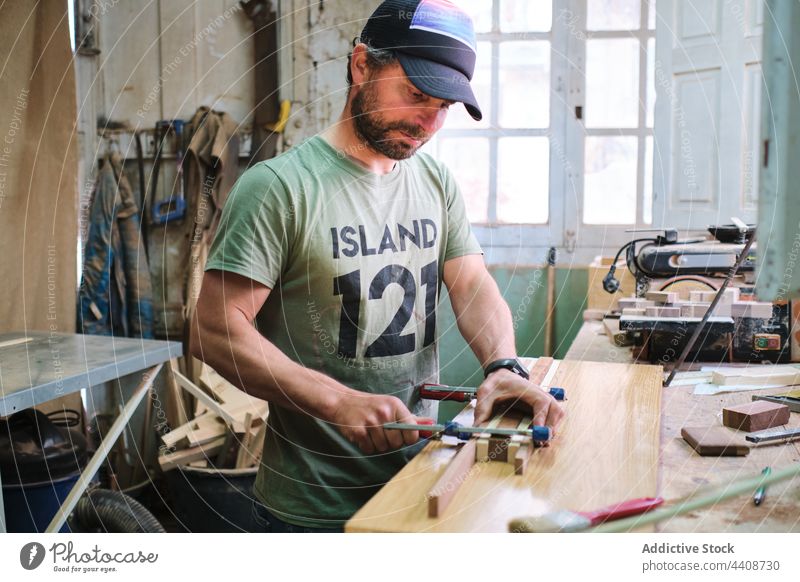 Fokussierter Schreiner beim Einspannen von Holzbrettern im Arbeitsraum Tischlerin einklemmen Schiffsplanken Leim achtsam Job präzise Werkzeug Beruf Mann