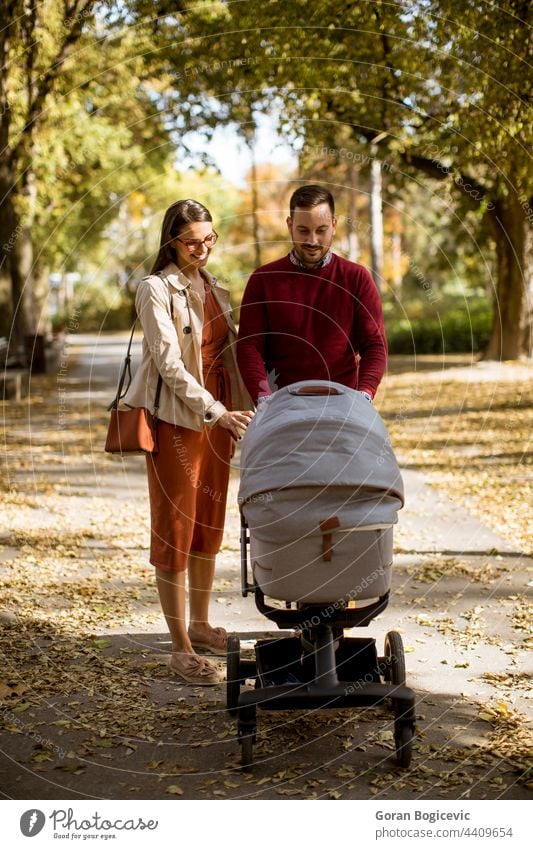 Glückliche junge Eltern, die im Park spazieren gehen und ein Baby im Kinderwagen fahren bezaubernd Herbst Wagen Kindheit Papa Familie Vater Freizeit Lifestyle