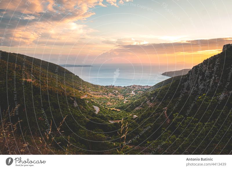 Fantastischer Sonnenuntergang auf der Insel Vis in Kroatien. Komiza Stadt in der Ferne. Goldene Stunde, orangefarbener Himmel und die wunderschöne blaue Adria. Grüne Berge umgeben die kleine malerische Stadt