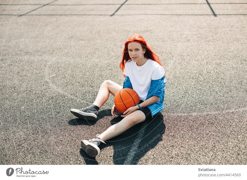 Ein charmantes junges Mädchen mit einem Basketball ruht sich nach einem Training aus. Ein Mädchen auf dem Sportplatz. Sport, Training, gesunder Lebensstil Ball