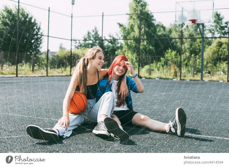 Zwei Mädchen in Sportkleidung und mit einem Basketball sitzen auf dem Spielplatz und unterhalten sich. Sport, Wettbewerb, Freundschaft Ball Teenager Gericht
