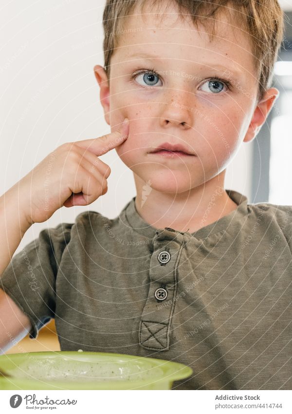 Niedlicher Junge am Tisch sitzend mit Essen beim Mittagessen Kind bezaubernd Mahlzeit Schalen & Schüsseln Lebensmittel heimwärts niedlich Wange berühren süß