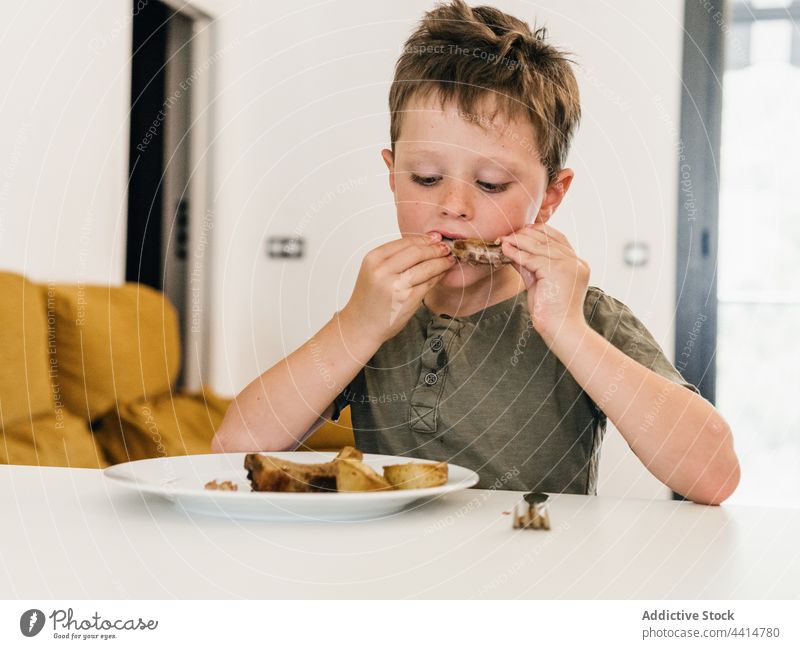 Hungriges Kind isst Schweinerippchen beim Mittagessen Schweinefleisch Rippe heimwärts Lebensmittel Junge appetitlich niedlich Mahlzeit bezaubernd genießen