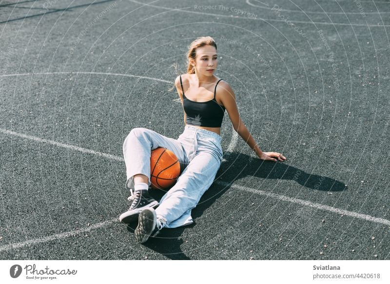 Ein Basketballspieler sitzt auf einem Sportplatz mit einem Basketball und schaut weg. Sport, Fitness, Lebensstil Mädchen Ball Spieler Spielplatz Sitzen jung