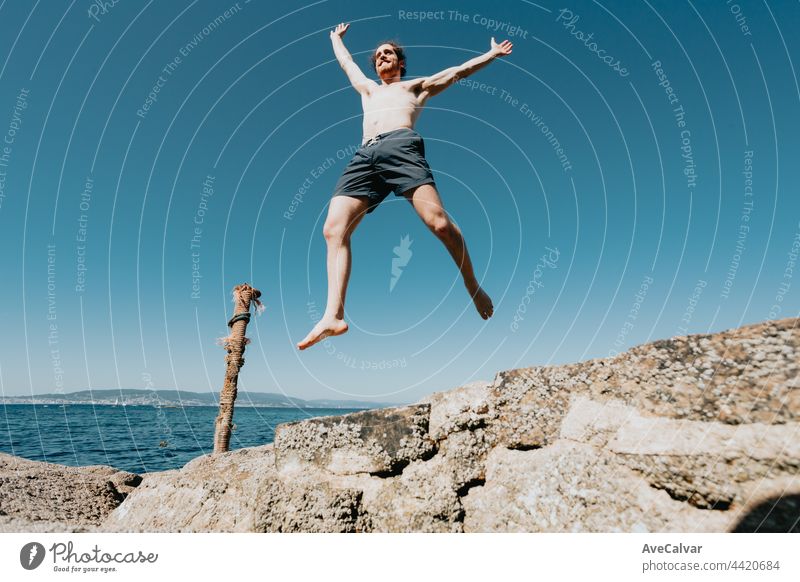 Junger Mann mit langen Haaren springt in die Luft, ohne Hemd an einem sonnigen Tag, Raum und Freiheit Konzept, Urlaub, fantastisches Bild, Strand Tag horizontal