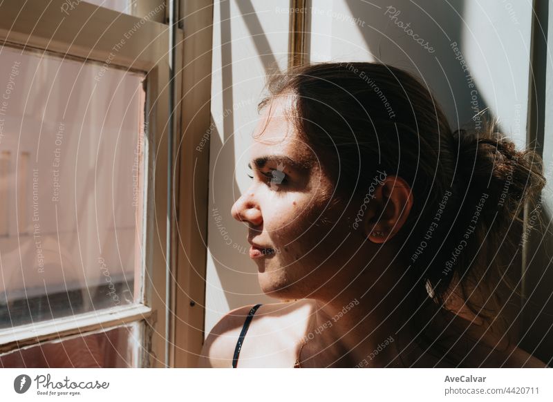 Junge Frau schaut durch ein Fenster während eines super sonnigen Tages, Kopie Raum, Reflexion und Denken Konzept, traurig und Angst, Selbstfürsorge Einsamkeit